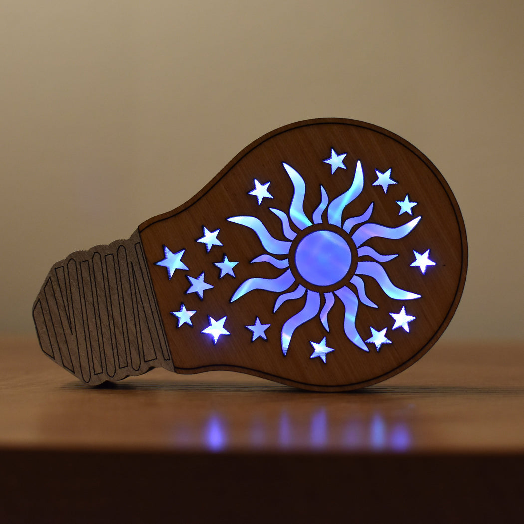 Decorative light bulb-shaped object with a sun and star design on a wooden surface.