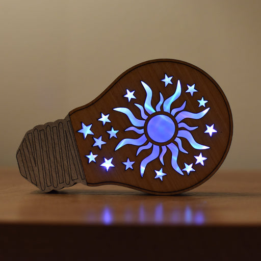 Decorative light bulb-shaped object with a sun and star design on a wooden surface.