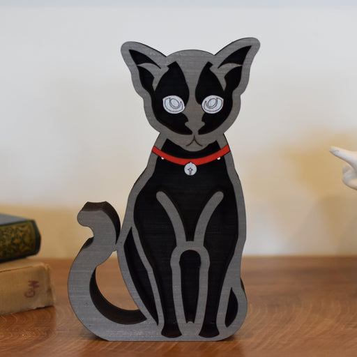 Black and gray cat figurine with a red collar on a wooden surface.