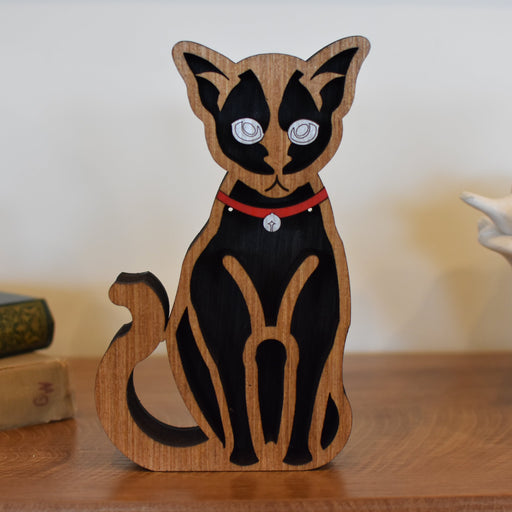 Wooden cat figurine with black and brown design on a wooden surface.