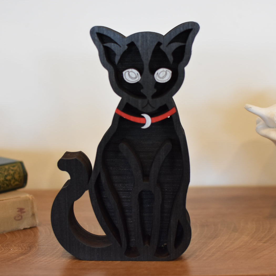 Black cat figurine with a red collar on a wooden surface
